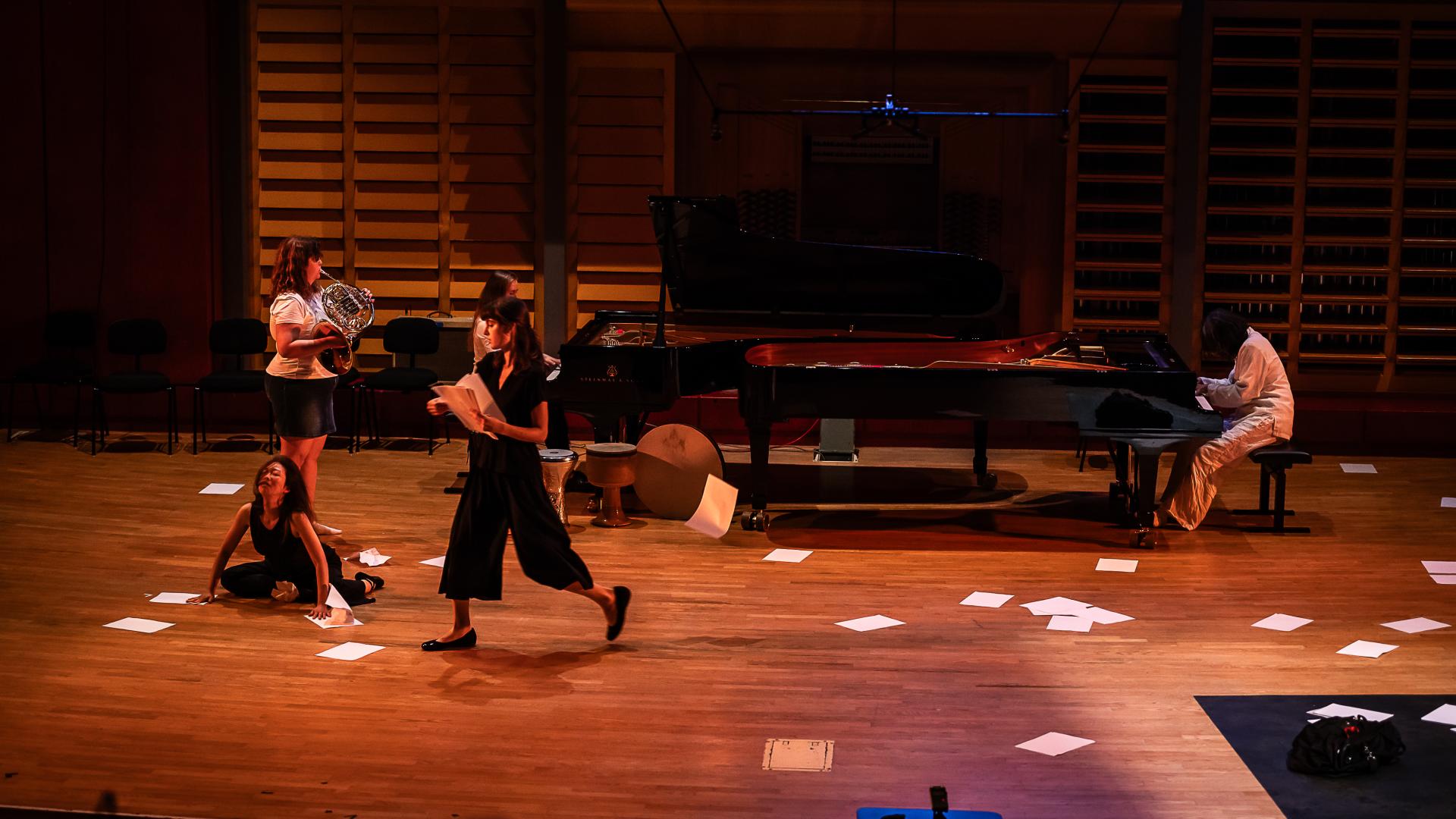 Papier liegt auf dem Boden, zwei Studierende an zwei Flügeln sitzen einander gegenüber.