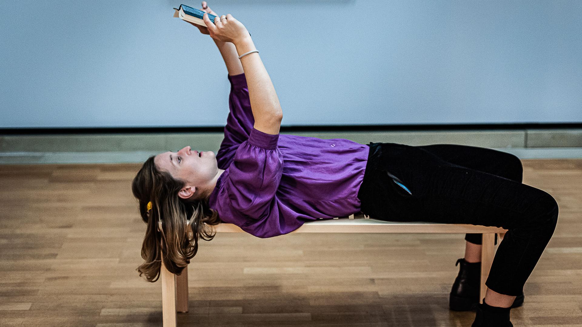 Sprechkunst-Studierende liegt mit dem Rücken auf einer Holzbank und hält ein Buch über sich.