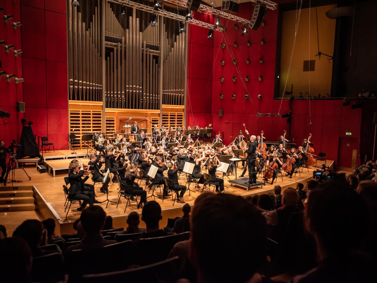 Das Hochschulsinfonieorchester im Überblick auf dem Konzertsaalpodium vor der angestrahlten Rieger-Orgel.
