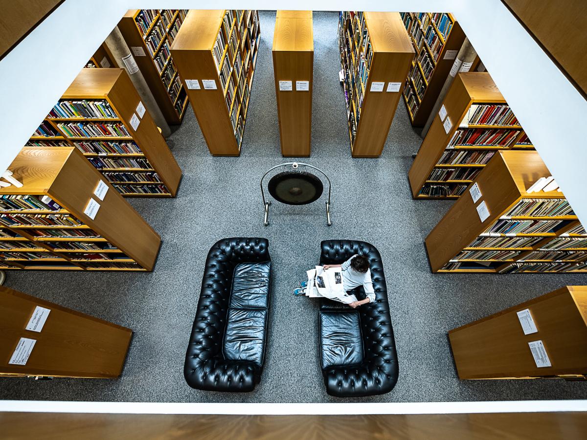 Auf dem Bild ist das untere Stockwerk der Bibliothek mit Sofas, Regalen und dem Gong zu sehen.