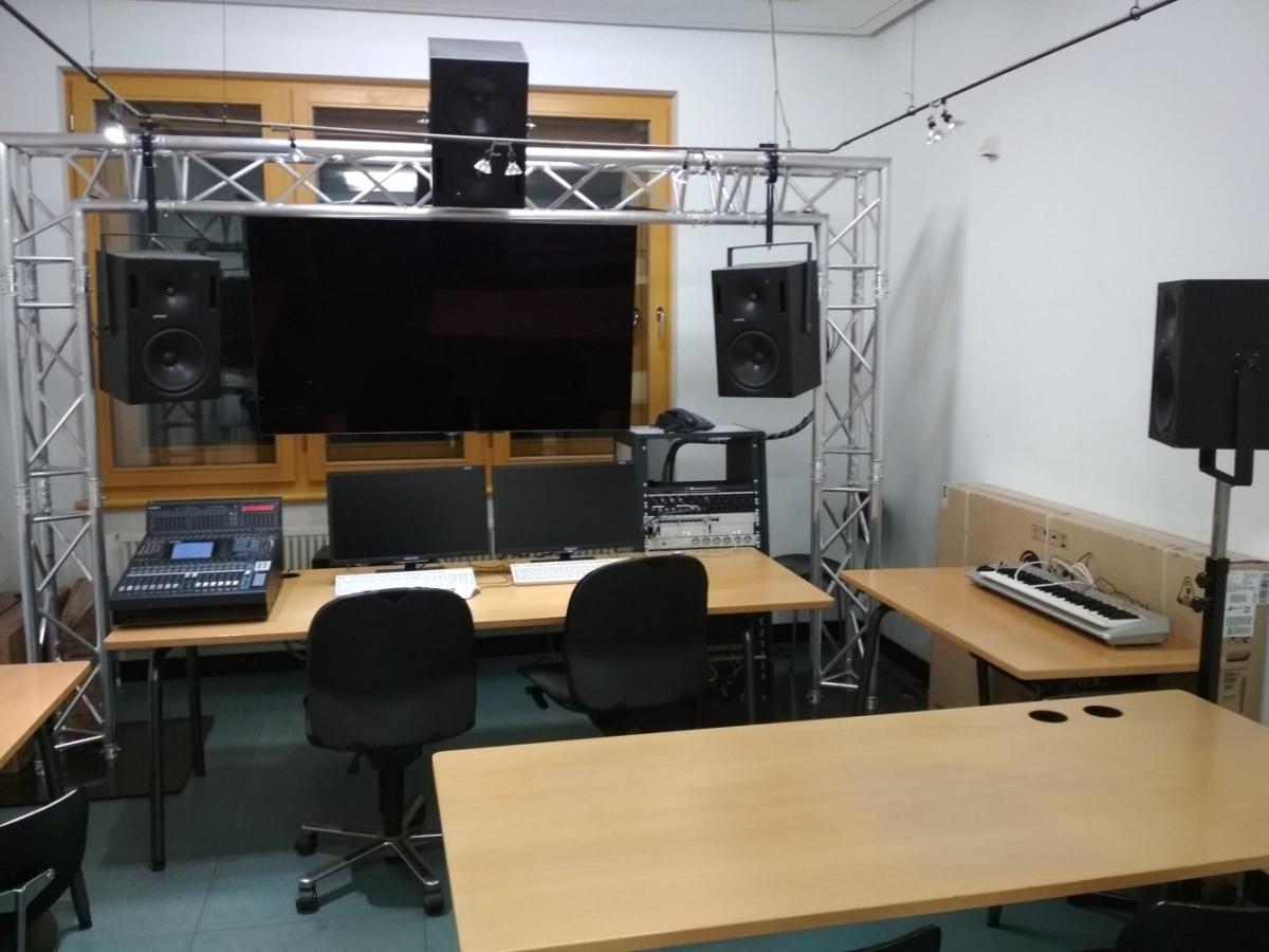 Ein großer Screen hängt über dem Schreibtisch, seitlich sind Mischpulte, Lautsprecher, Monitore und Keyboards installiert.