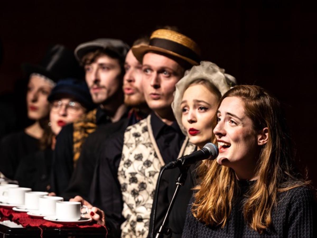 sieben Menschen singen verkleidet auf Bühne.