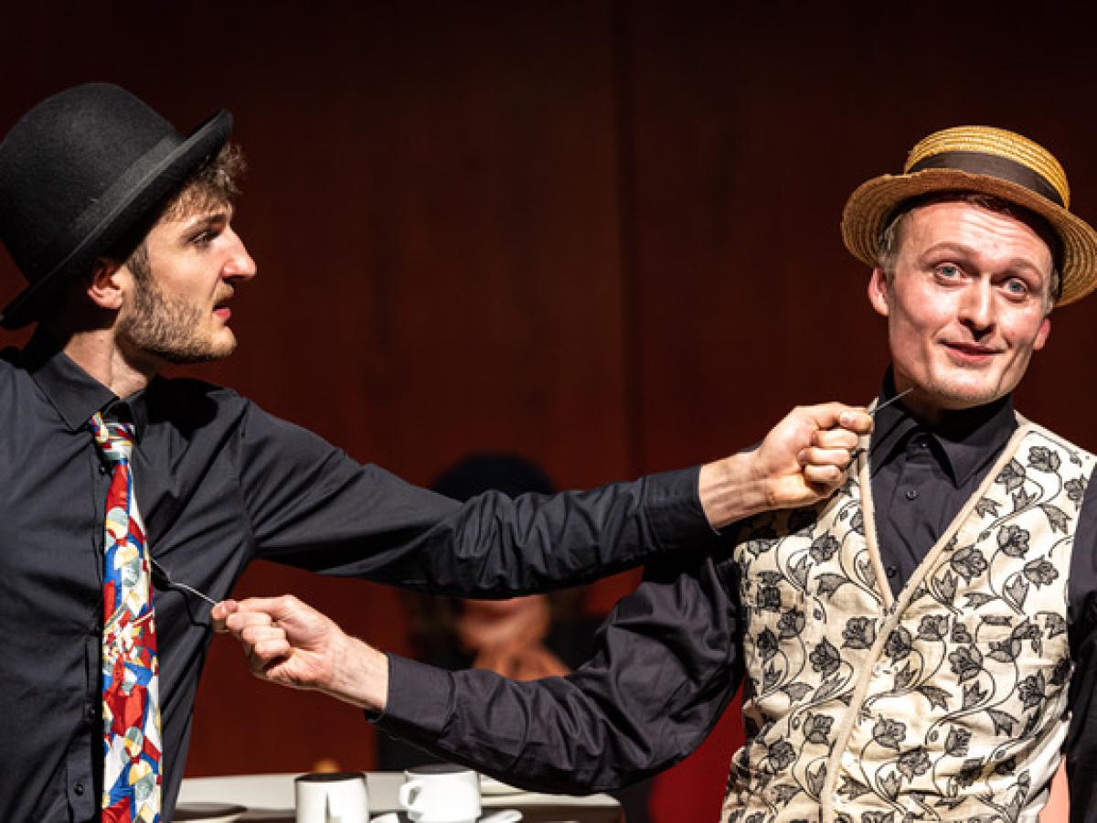 Zwei Männer mit Hüten bedrohen sich gegenseitig mit Löffeln.