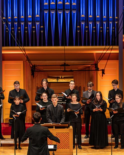 Das zwanzigköpfige Vokalensemble auf dem Konzertsaalpodium. In der Mitte begleitet Johannes Friederich das Ensemble auf der Truhenorgel.n der Tr