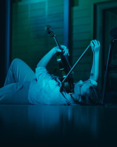 Eine junge Frau spielt Geige, während sie auf dem Boden liegt.