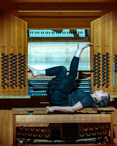 Studentin liegt mit dem Rücken auf dem Orgelbank des Konzertsaales und streckt ihre Beine von sich.