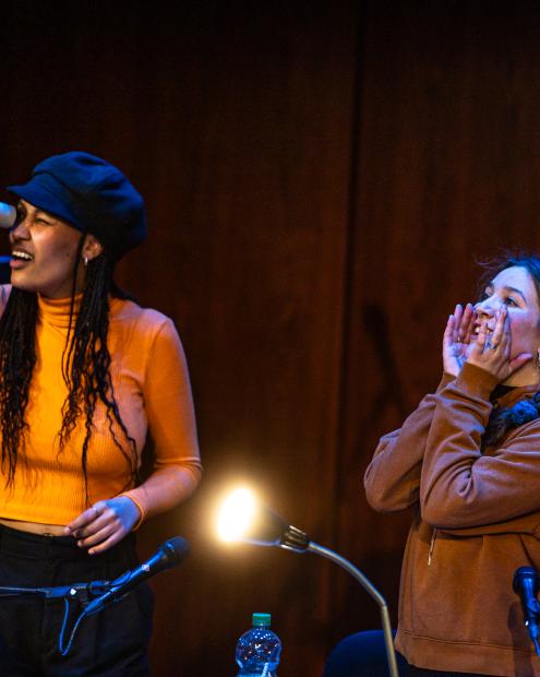 Zwei Frauen richten ihren Blick in den Zuschauerraum. Die eine mit einem imaginären Fernrohr, die andere umgibt mit ihren Händen den Mund als Schalltrichter.