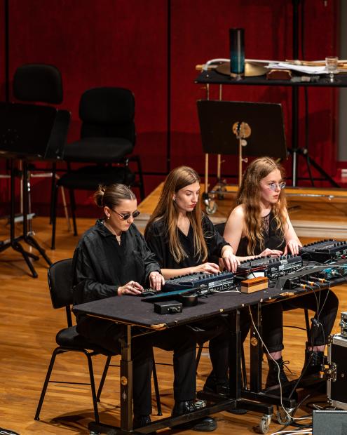 Dret Studierenden sitzen an einem Tisch mit unterschiedlichen Pulten. An einem gesondert Tisch sitzt eine Studierende mit Keyboard. Zwischen den Tischen sind Dutzende von Kabeln verlegt.