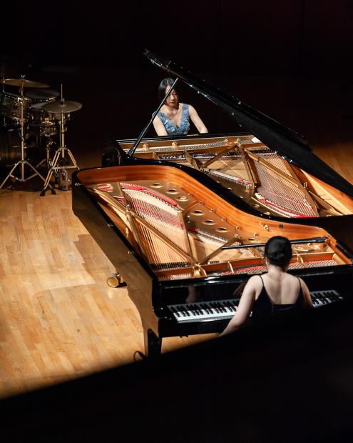 Aus der Vorgelperspektive sind beide Konzertflügel, zwei Pinaistinnen und ein Schlagzeugaufbau im Hintegrund zu sehen. 