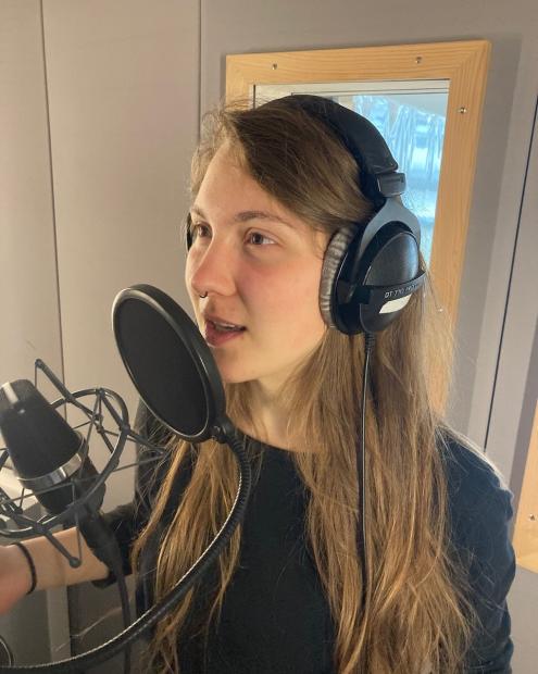 Studentin spricht in Sprechkabine mit Kopfhörern in ein Mikrophon.