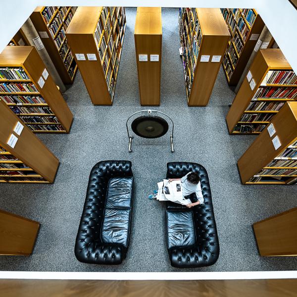 Auf dem Bild ist das untere Stockwerk der Bibliothek mit Sofas, Regalen und dem Gong zu sehen.