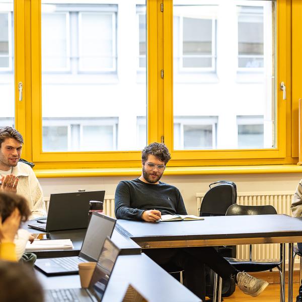 Studierende in einer Seminarsituation im Gespräch mit Prof.in Dr. Karolin Schmitt-Weidmann. Auf den Tischen befinden sich verschiedene Laptops und Tablets.