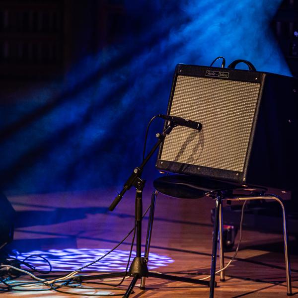 Ein Gitarrenverstärker steht auf einem Stuhl auf einer Bühne im Scheinwerferlicht.