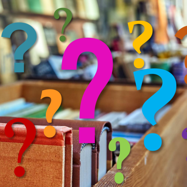 Das Bild zeigt bunte Fragezeichen vor bunten Büchern in Holzkisten