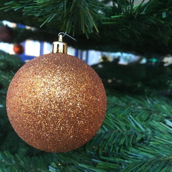 Das Bild zeigt eine goldene, glitzernde Kugel an einem Weihnachtsbaum.