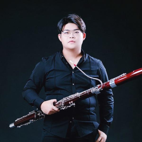 Ganzkörperfoto des Studenten Yi Yang mit seinem Fagott in der Hand vor sich.