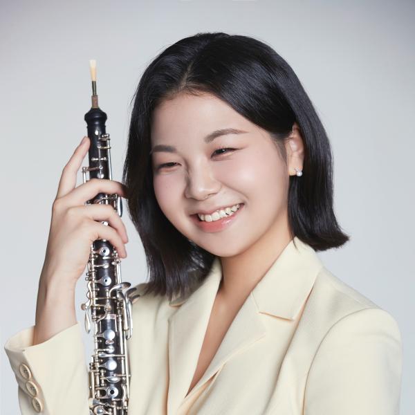 lachende Studentin mit mittellangen dunklen Haaren hält ein Englischhorn vor sich.