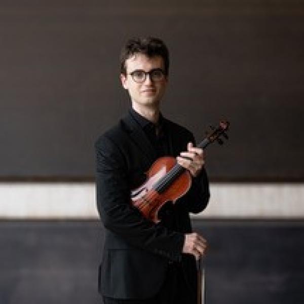 Der Student Ícar Solé Bachs steht mit seiner Violine unter dem Arm mittig vor einer Wand.