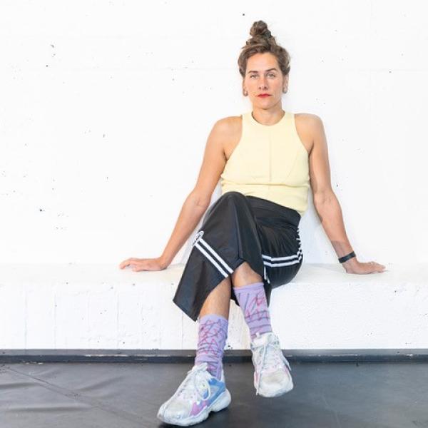 Die Stiudentin Magdalena Weniger sitzt mit einem Tanktop, einer Sporthose udn Turnschuhen mit überschlagenen Beinen auf einer Bank und stützt sich mit beiden Armen auf der Bank ab.