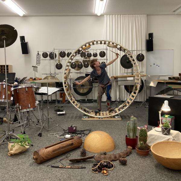 Der Alumnus Augustin Lipp steht in einem Raum voller Schlagwerkzeuge in einem Instrumentalrad.