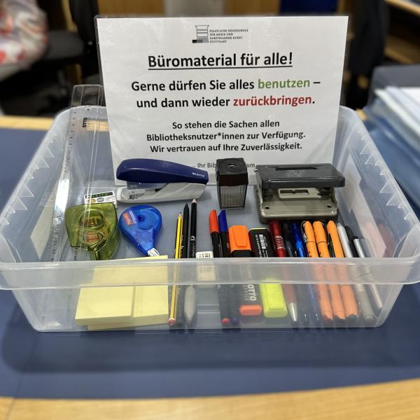 Transparente Plastikwanne mit unterschiedlichen Stiften, Haftnotizzetteln und weiterem Bürobedarf.
