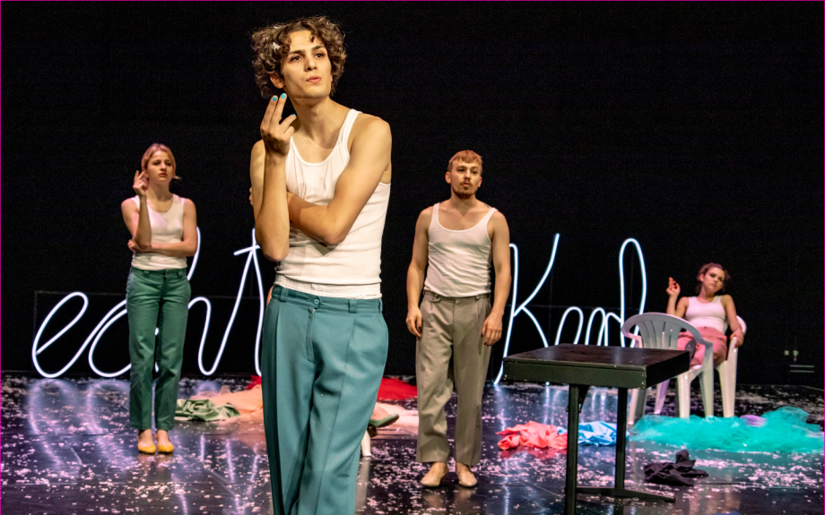 vier Menschen auf Bühne. Drei deuten an zu rauchen.