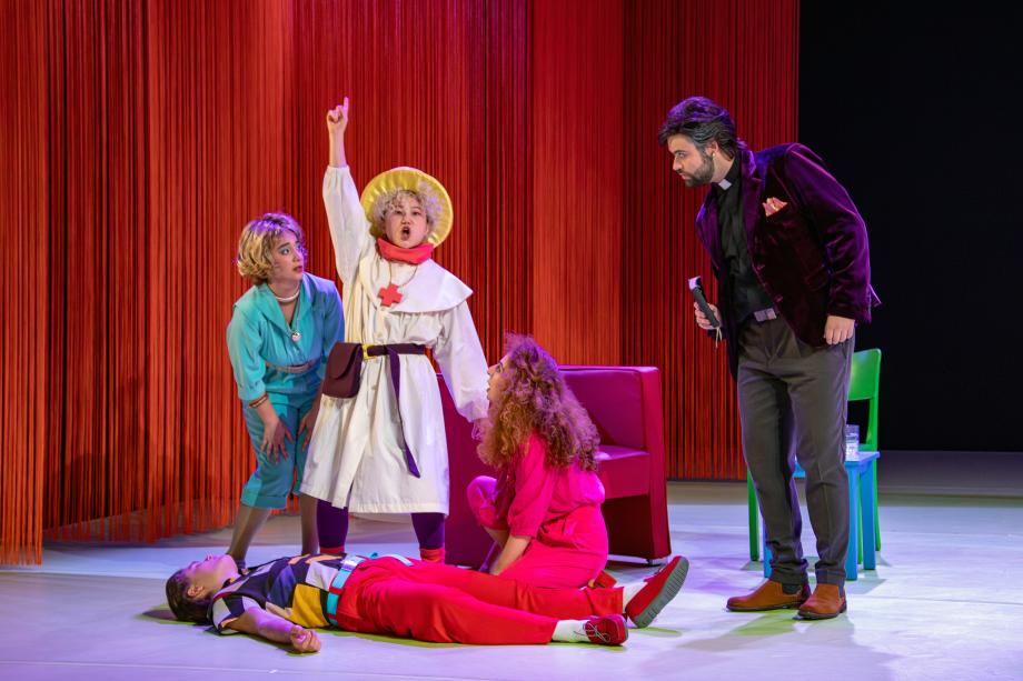 fünf Studierende auf der Bühne. Eine Studentin steht in der Mitte ruft und meldet sich. Zwei Studentinnen um sie herum schauen sie erschrocken an. Auf dem Boden liegt ein Student-scheinbar bewusstlos. Rechts, etwas abseits, steht ein Pfarrer und schaut zur Gruppe mit einer Bibel in der Hand.