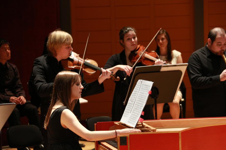 Eine Cembalistin im Fokus mit dahinter musizierenden Streichern.