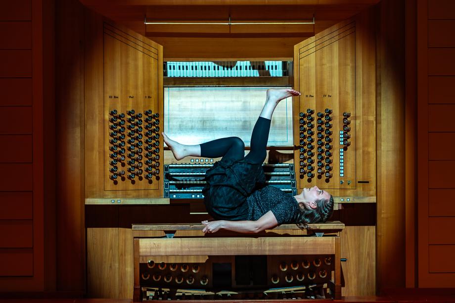 Studentin liegt auf dem Rücken auf der Orgelbank und streckt ihre Füße nach oben. Sie hat nackte Füße.