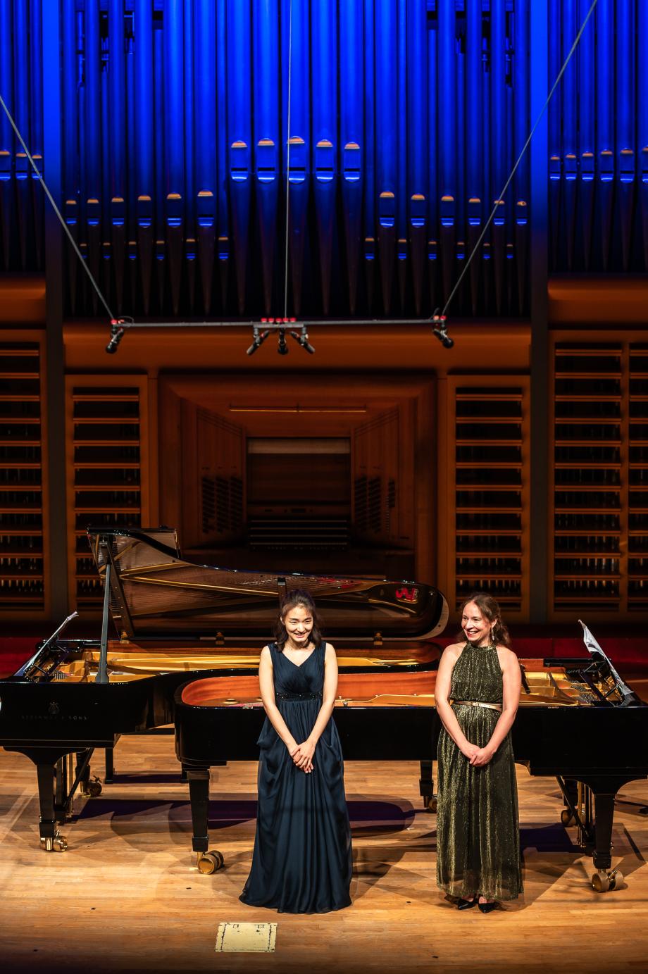 zwei Studierende in langen Kleidern vor Flügeln stehend.