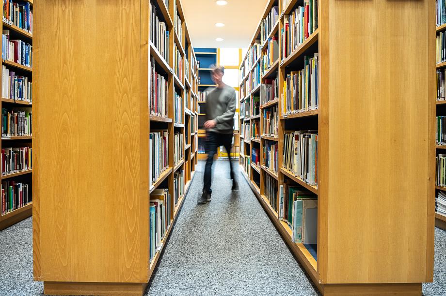 Das Bild zeigt eine Person zwischen Bibliotheksregalen.