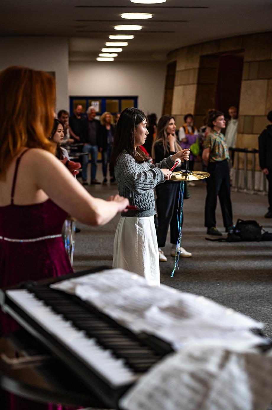 SChlagzeugstudierende performen im Konzertsaalfoyer, den Blick auf die Glasfront gerichtet.