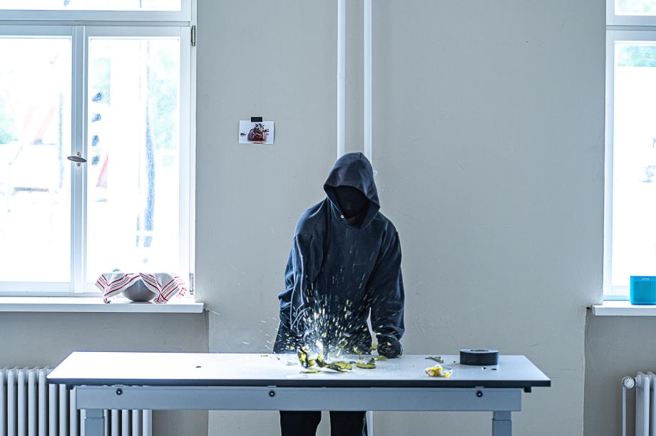 Schwarz bekleideter Studierende zertrümmert mit dem Hammer eine Flasche.