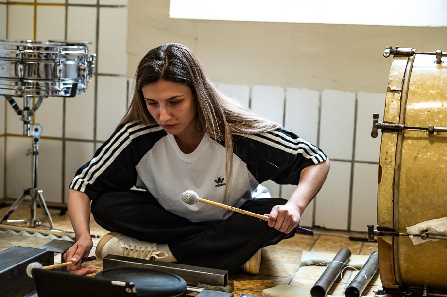SChlagzeugstudierende performt im Schneidersitz auf einem gefliesten Boden.