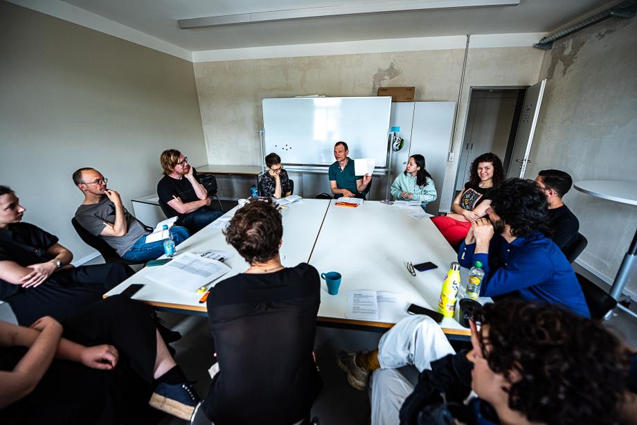 Ein Gruppe aus Studierenden und Lehrenden sitzt um zwei Kongresstische und diskutiert.