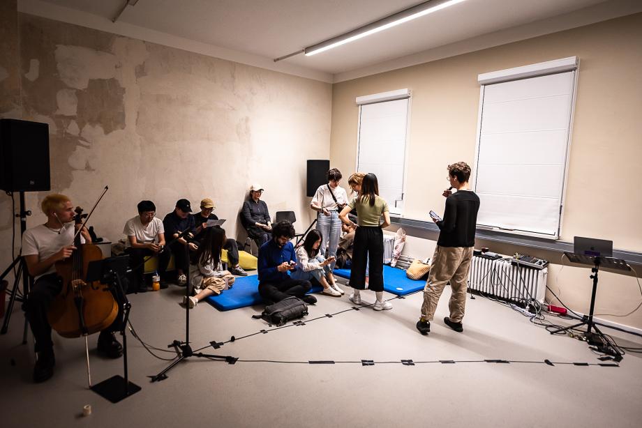 Ein sehr neutraler Raum mit verschiedenen Menschen. Ausführende und Zuschauer lassen sich nicht unterscheiden.