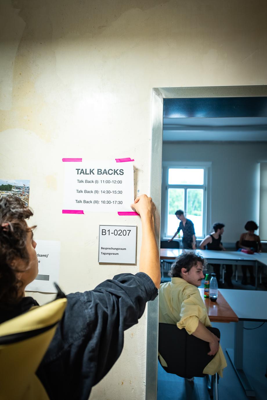 Eine Person klebt einen Programmzettel vor ein Zimmer.