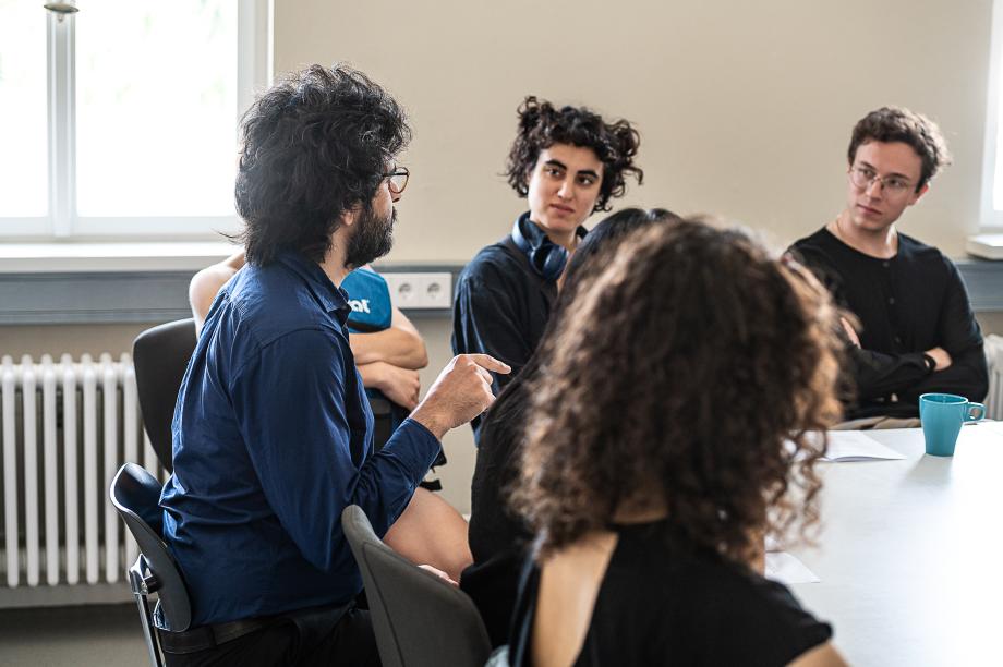 Menschen dikutieren in einem Raum an einem Tisch sitzend.