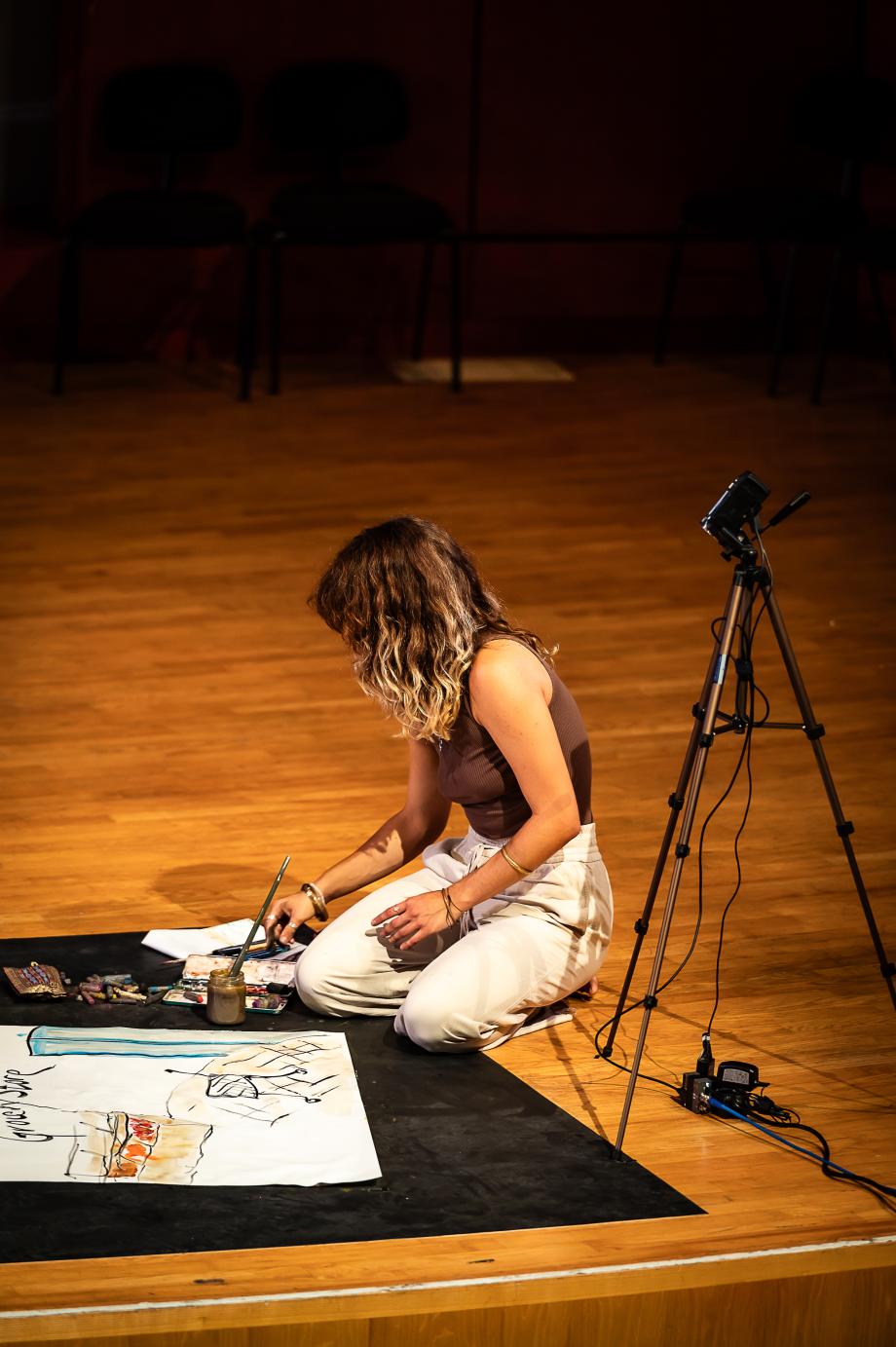 Studentin sitzt auf Boden und malt mit Aquarell.