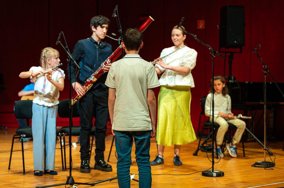 Musizierende Kinder auf dem Podium. Im Vordergrund steht ein Junge, der das Ensemble leitet.