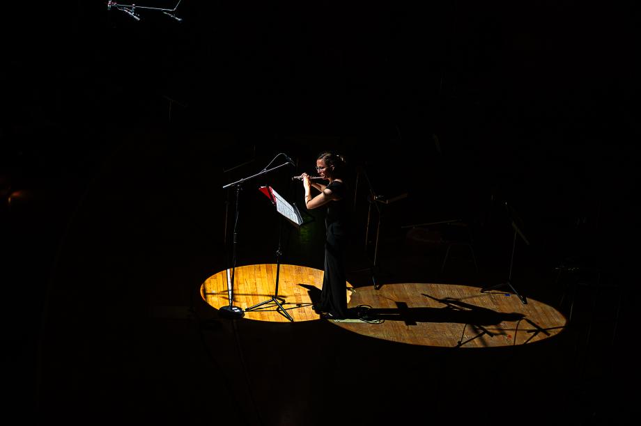 Karolin Schmitt-Weidmann konzertiert als Flötistin in der Bühnenmitte. Nur ein heller Lichtkegel von oben beleuchtet sie. 