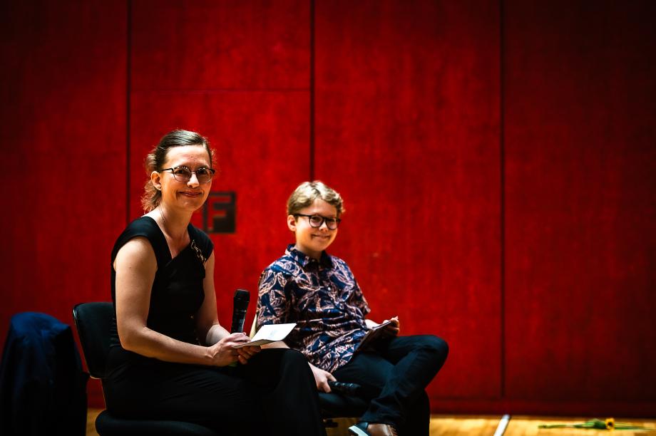 Karolin Schmitt-Weidmann im Gespräch mit ihrem Sohn, der als Gesprächspartner auf dem Podium fungiert. Beide sitzen und wenden ihren Blick auf den beobachtenden Fotografen.