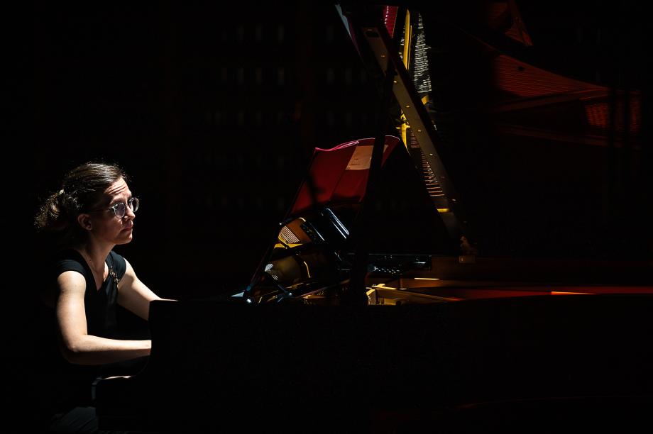 Karolin Schmitt-Weidmann konzertiert am Flügel. Der Fokus ist auf ihre Körpersprache gerichtet. Die BEleuchtungssituation ist sehr dunkel. Im Hintergrund wird das Orgelprospekt leicht illuminiert.