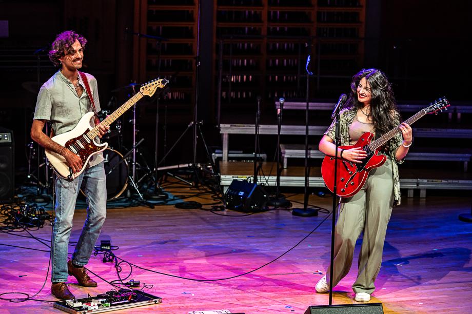Schulmusikkonzert 2024:Ein student und eien Studentin an E-Gitarren am Mikrophone. Beide lachen.