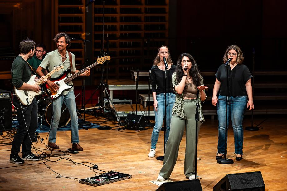 Schulmusikkonzert 2024: links zwei Studenten mit E-Gitarren, rechts: drei Studentinnen, die singen.