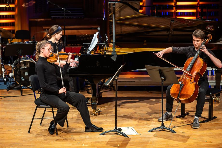 Schulmusikkonzert 2023: Im Hintergrund Studentin am Flügel. Im Vordergrund: zwei Studierende mit Violine und Cello.