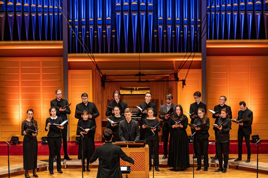 Das Studiovokalensembles unter der Leitung eines Studierenden. Der Organist an der Truhenorgel steht im Blickkontakt mit dem Ensembleleiter.