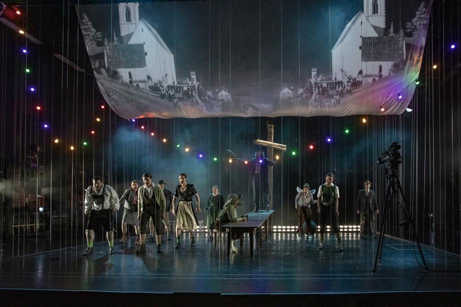 Studierende der Opernschule in einer Bühnenszene. Alle schauen angespannt nach vorne, im Hintergrund befindet sich ein Kreuz.