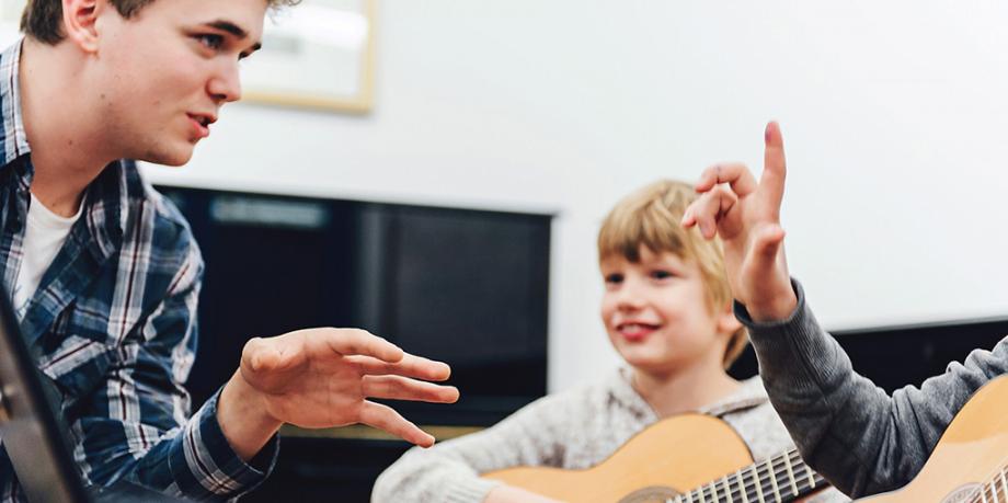 Studierende sprechen miteinander. Im Hintergrund Kind mit Gitarre.