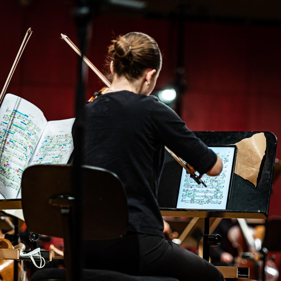 Blick von hinten auf ein Notenpult einer Geigerin. Auf dem Pult liegt ein Tabletpad und abgerissenes Schleifpapier.
